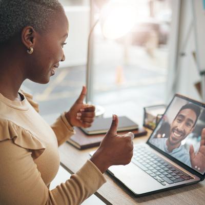 A black woman in an office happily putting two thumbs up during a video call.