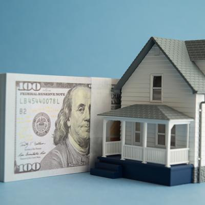 A house miniature and U.S. dollar banknotes in a blue background.