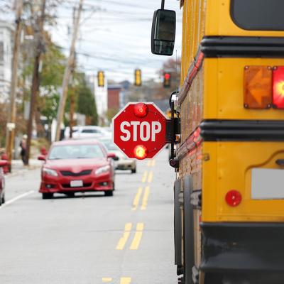 Rear view of a school bus with a 'stop' sign being held by its driver.