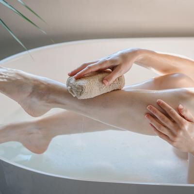 A cropped view of a person washing her legs in a bath tub with a body sponge.