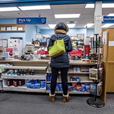 Woman in a winter coat purchasing medication at a CVS pharmacy counter.