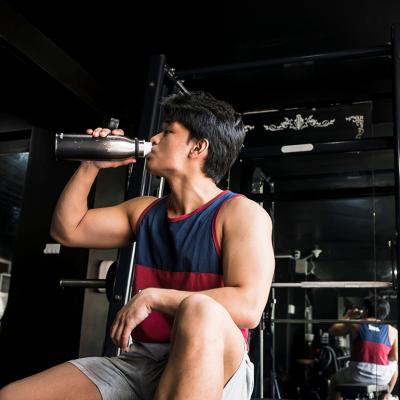 A young, fit man drinking water inside a gym.
