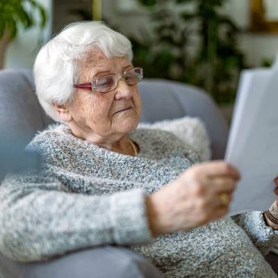 A senior woman reading documents while sitting in an armchair in a living room.