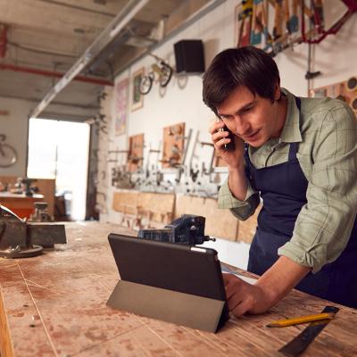A male bicycle small business owner on the phone while reviewing information on a laptop in a workshop.