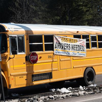 A school bus with a hanging display of drivers needed during a driver shortage in Windsor, New York, USA.