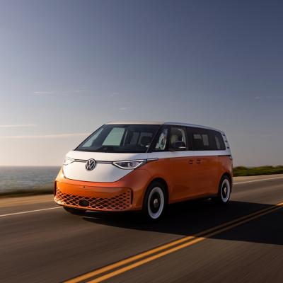 Candy White over Energetic Orange 2025 Volkswagen ID Buzz driving on road next to ocean.
