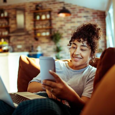 A young woman at home smiling at her phone while relaxing on a couch.