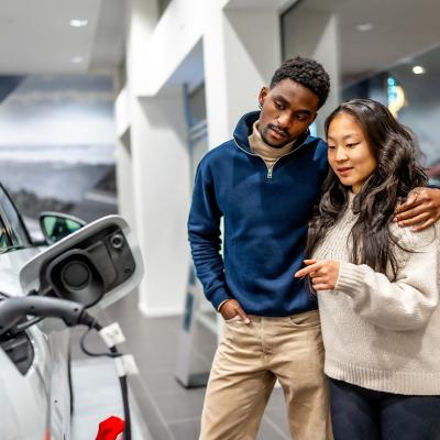 A multiethnic couple examining the charging port of an electric vehicle at a car dealership.