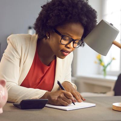 A black businesswoman writing notes beside a piggy bank as a concept of budgeting.