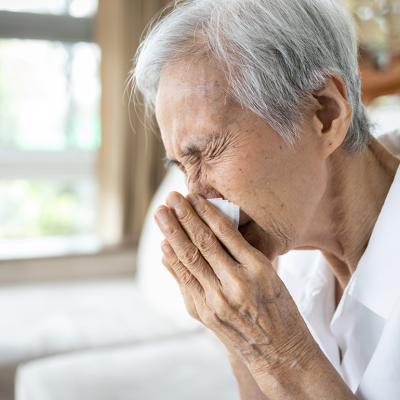 An elderly person blowing her nose after a sneeze.
