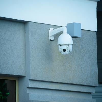 A view of a security camera on the facade of a gray building.