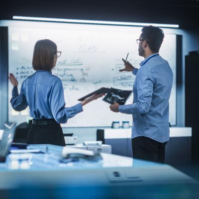 A team of two professional engineers using a digital tablet to discuss a manufacturing plan.