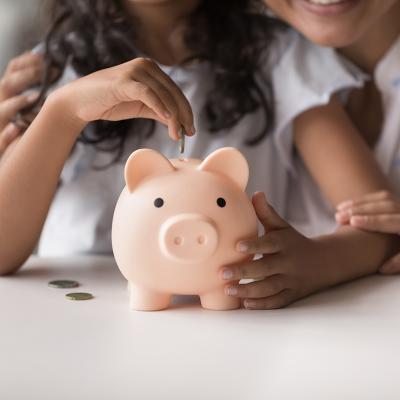 Mother helps daughter put coins in a piggy bank.