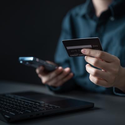 A person checking credit card details from a smartphone and laptop.
