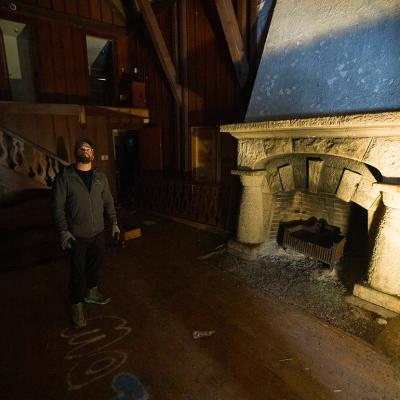 Cameron Jensen standing inside one of his newly acquired buildings in Logan Canyon in front a fireplace illuminated by a floor lamp.