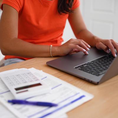 A woman organizing finances at home using a laptop and calculator over documents.