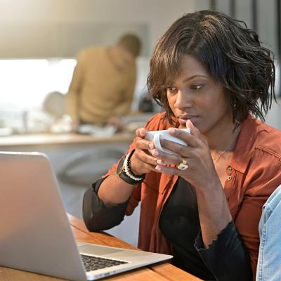 A black woman working from home and sipping a cup of coffee.