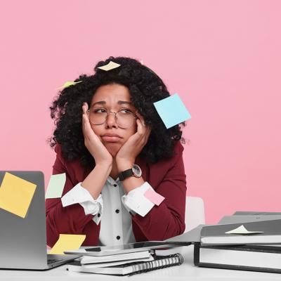 A young woman with sticky notes taped around her looking stressed at work.