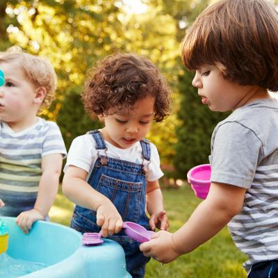 Three little children playing around a water table in a garden.