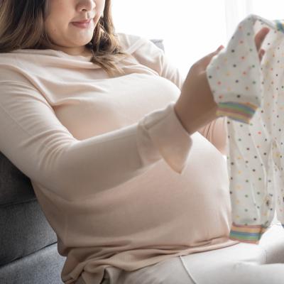 A pregnant woman checking on new baby clothes at home. 