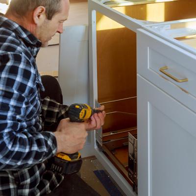 A woodworker installing a drawer for a garbage bin in a kitchen.