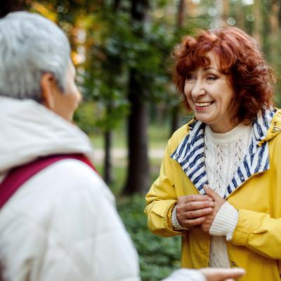 Two elderly female friends having a conversation out in the woods.