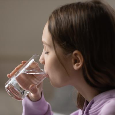 A young dehydrated teenage girl drinking a glass of water.