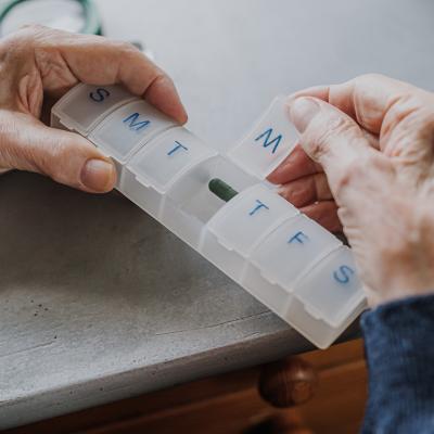 An elderly person arranging medicine in a pill box for the week.