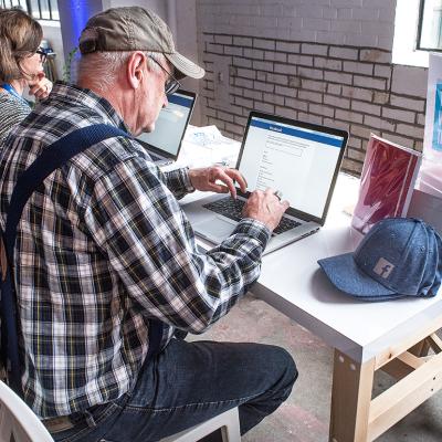 A senior man signing up for a Facebook account at a community boost event.