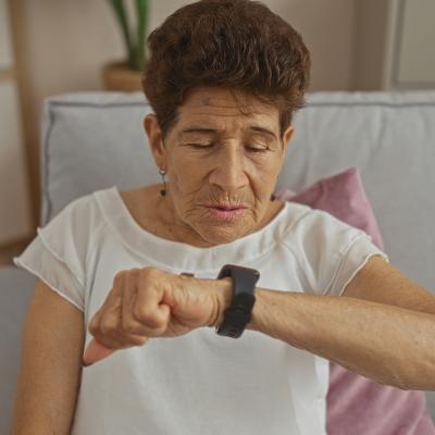 A senior woman observing her smartwatch while sitting on a sofa at home.