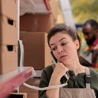 A warehouse worker talking over the landline phone about package shipment.