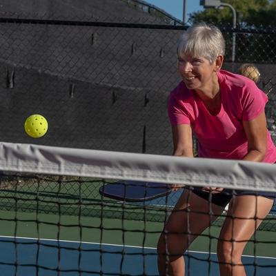 An elderly person enjoying a good time while playing pickleball in a court.