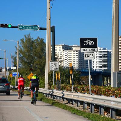 Two cyclists travel north in a bike lane toward the Real Intracoastal Waterway Bridge in Florida, USA.