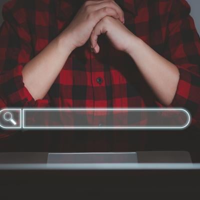 A floating search bar and a data analyst working on search engine concept from a laptop in the background.