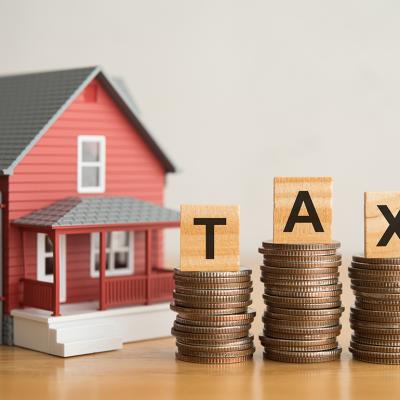 A miniature house and stacks of coins under TAX alphabet blocks.