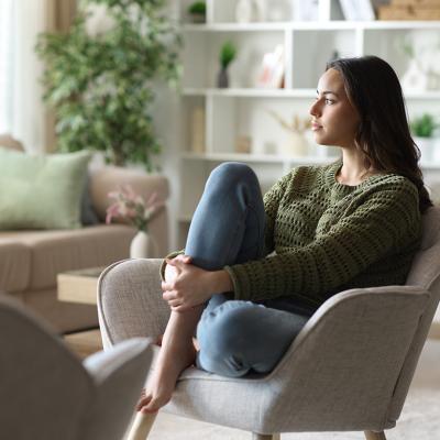 A woman sitting at home pensively looking out the window.