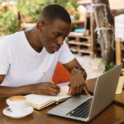 A young male student focused on working with a laptop in an outdoor cafe.