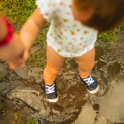 A toddler holding mother's hand while playing in a mud puddle.