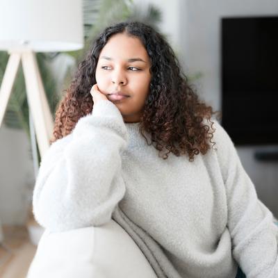 A pensive young woman sitting on the couch at home.