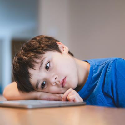 A bored young child staring at a tablet.