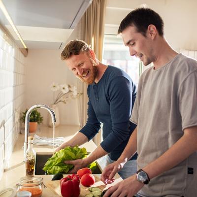 A young gay male couple preparing vegetables in their home's kitchen.