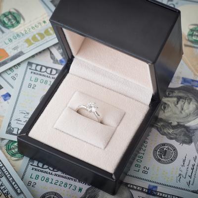 A diamond engagement ring placed above U.S. dollar bills.