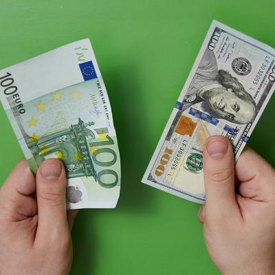 100 Euro and 100 dollar bills held by a person's hands in a green background.