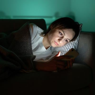 A person surfing internet from her smartphone in a dark room at night.