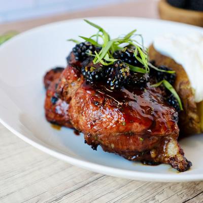 A plate of savory grilled porkchop dish with berry sauce and potatoes.