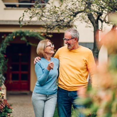 A senior couple happily standing in front of their new home.