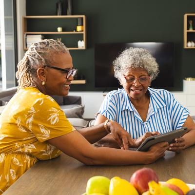 Two senior women sharing to use a tablet in their living room.