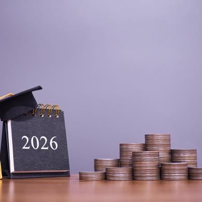 A 2026 calendar with a graduation hat and stacks of coins in a desk.