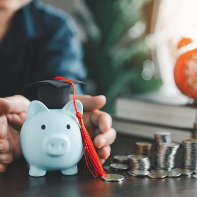 Person protecting a piggy bank with a graduation cap as a concept of saving money for education.