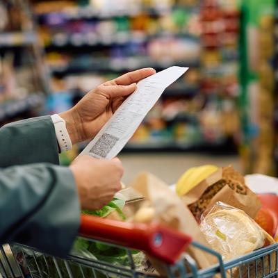 Person looking at a long grocery shopping bill while still at a supermarket.